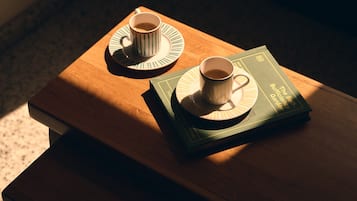 Un tavolo di legno con due tazze di caffè sui piattini e un libro intitolato 'The Sufficient Self-Garden'.