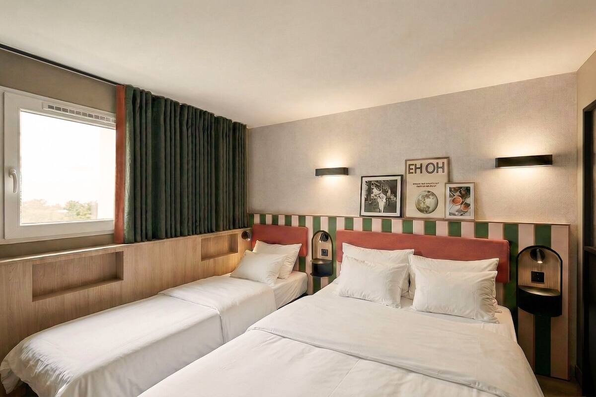 A hotel room with two beds, a window, a wall-mounted picture, and a nightstand.