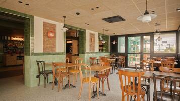Een restaurantinterieur met houten tafels en stoelen, een wand betegeld met groene tegels en een uitzicht door grote ramen.