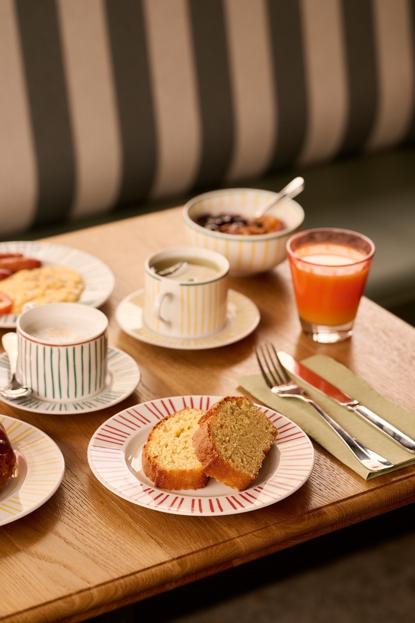 A breakfast setting with a plate of bread, a cup of coffee, a glass of orange juice, and a bowl of cereal on a wooden table.