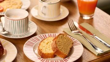 A breakfast setting with a plate of bread, a cup of coffee, a glass of orange juice, and a bowl of cereal on a wooden table.