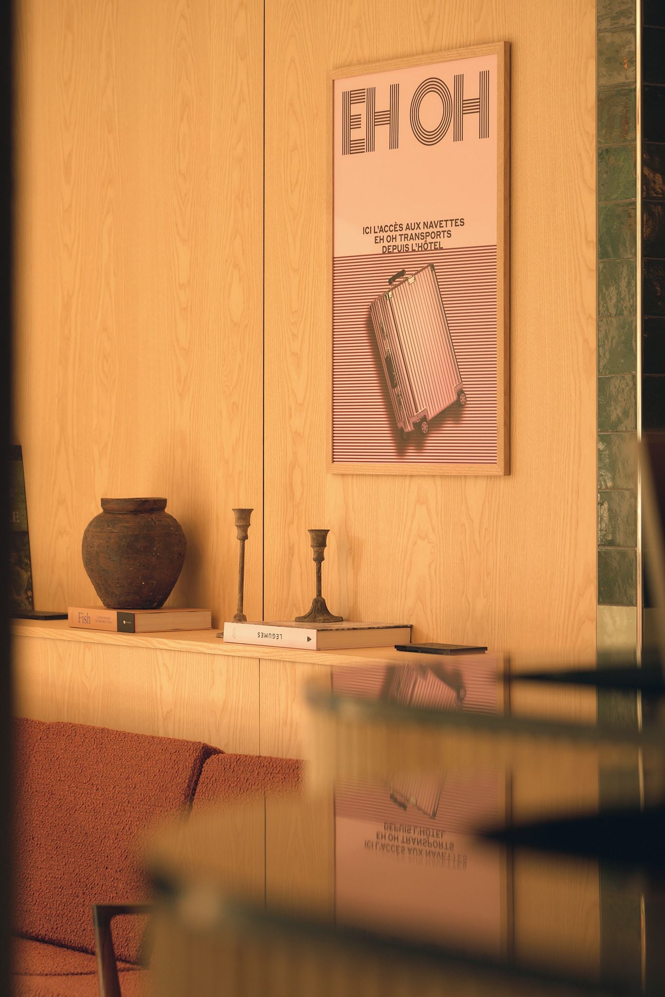 Un mur en bois orné d’une affiche encadrée représentant des bagages et du texte, ainsi qu’un vase, des chandeliers et des livres placés sur une étagère.