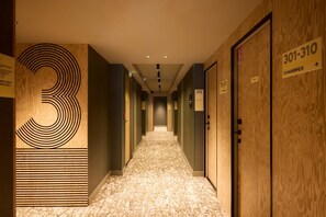A hotel corridor with wooden doors, numbered room signs, and a carpeted floor. - Hôtel EH OH Orly Rungis (Rungis)