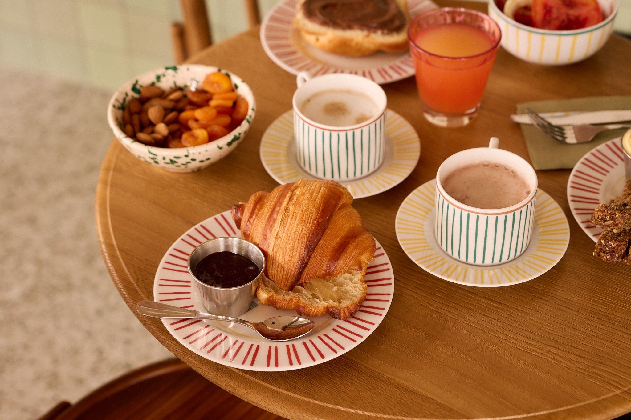 A breakfast setting with croissants, jam, coffee, and juice on a wooden table.