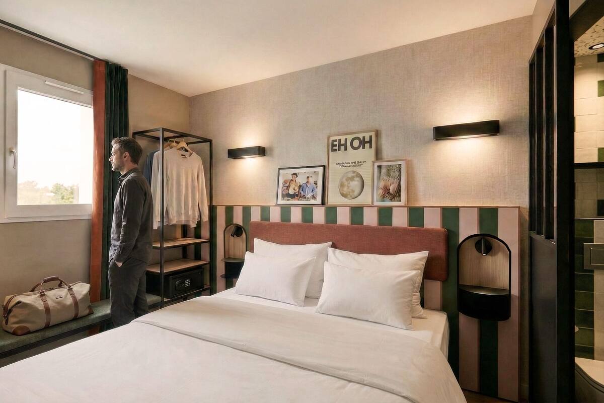 A hotel room with a bed, a desk with a laptop, a wardrobe, and a window.