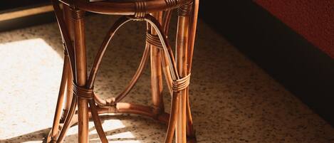 A wicker stool with a book on it, positioned near a bookshelf and a cushioned bench.