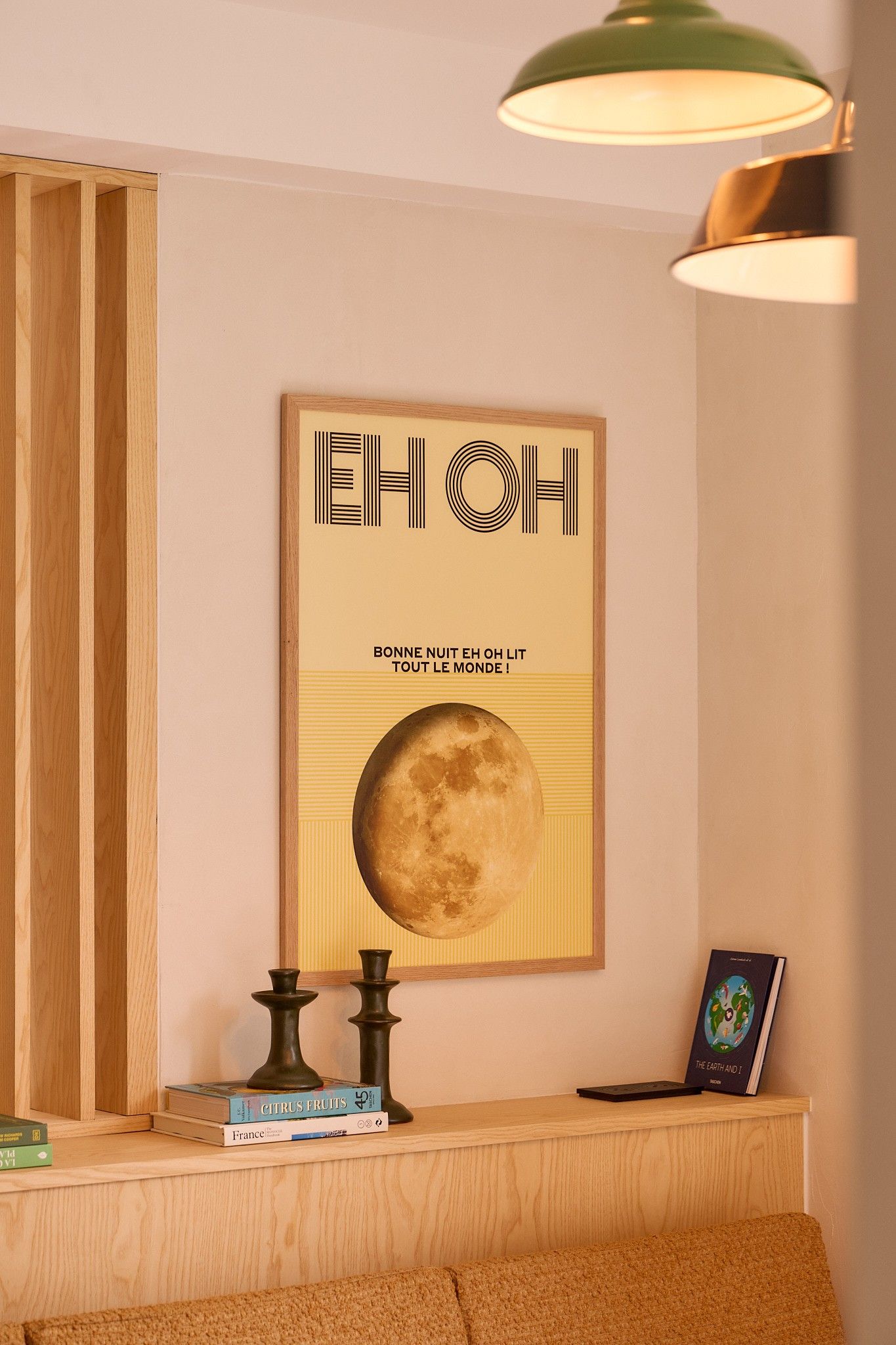 Une pièce avec une affiche de la lune encadrée, une bibliothèque remplie de livres, une lampe et une petite table.
