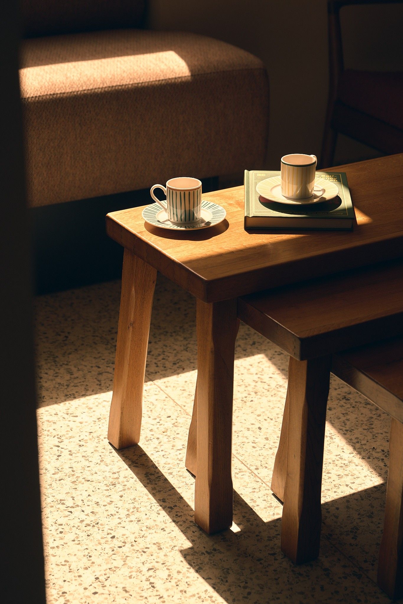 Una mesa de madera con una taza, un platillo y un libro encima.