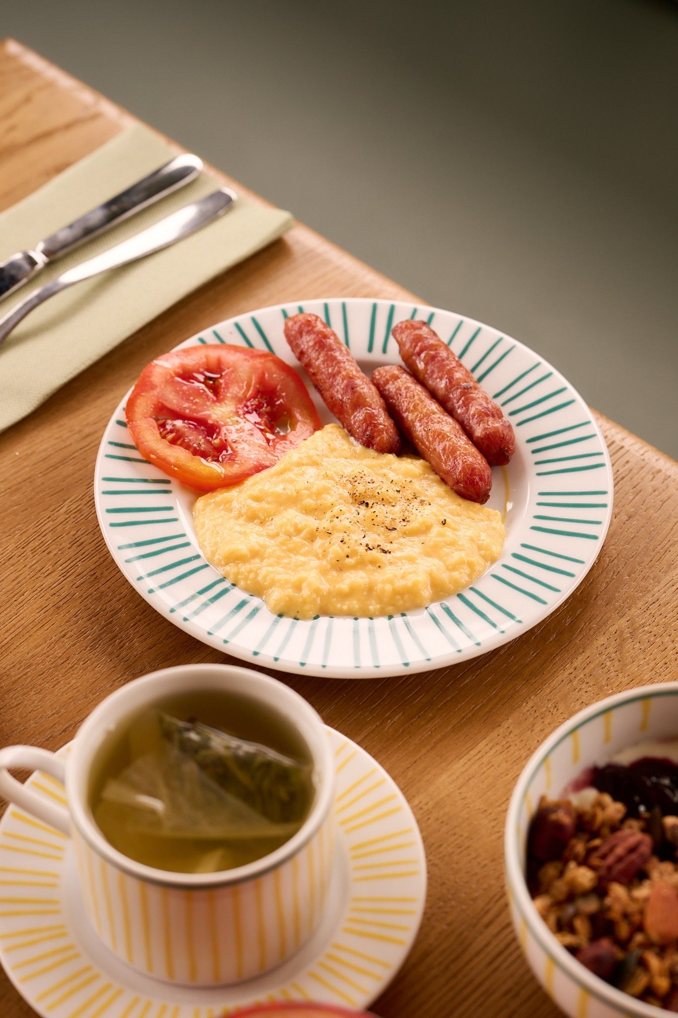Une assiette avec des œufs brouillés, des saucisses et une tranche de tomate, le tout présenté sur une assiette à rayures.