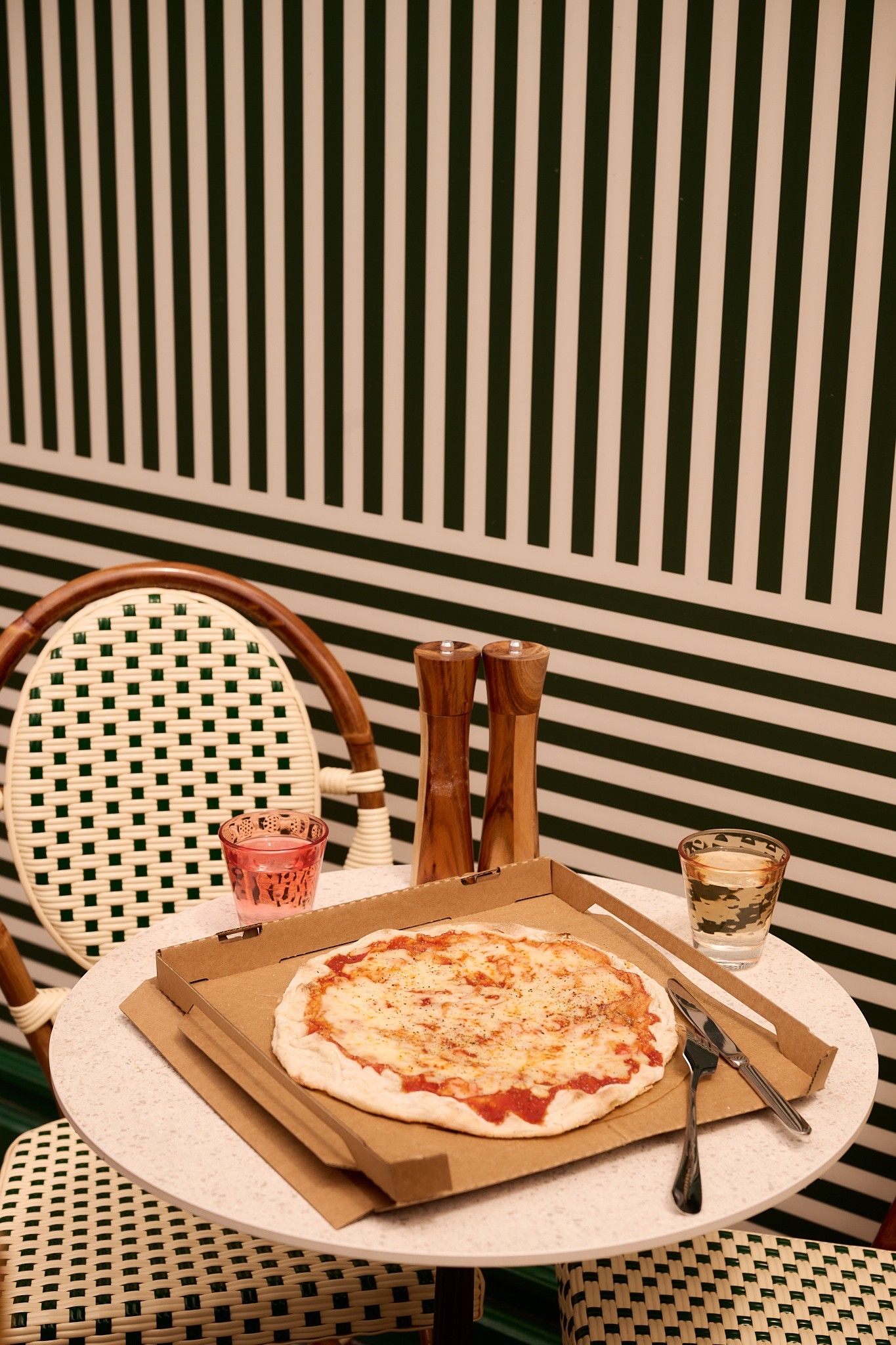 A pizza in a cardboard box on a round table with a striped background.