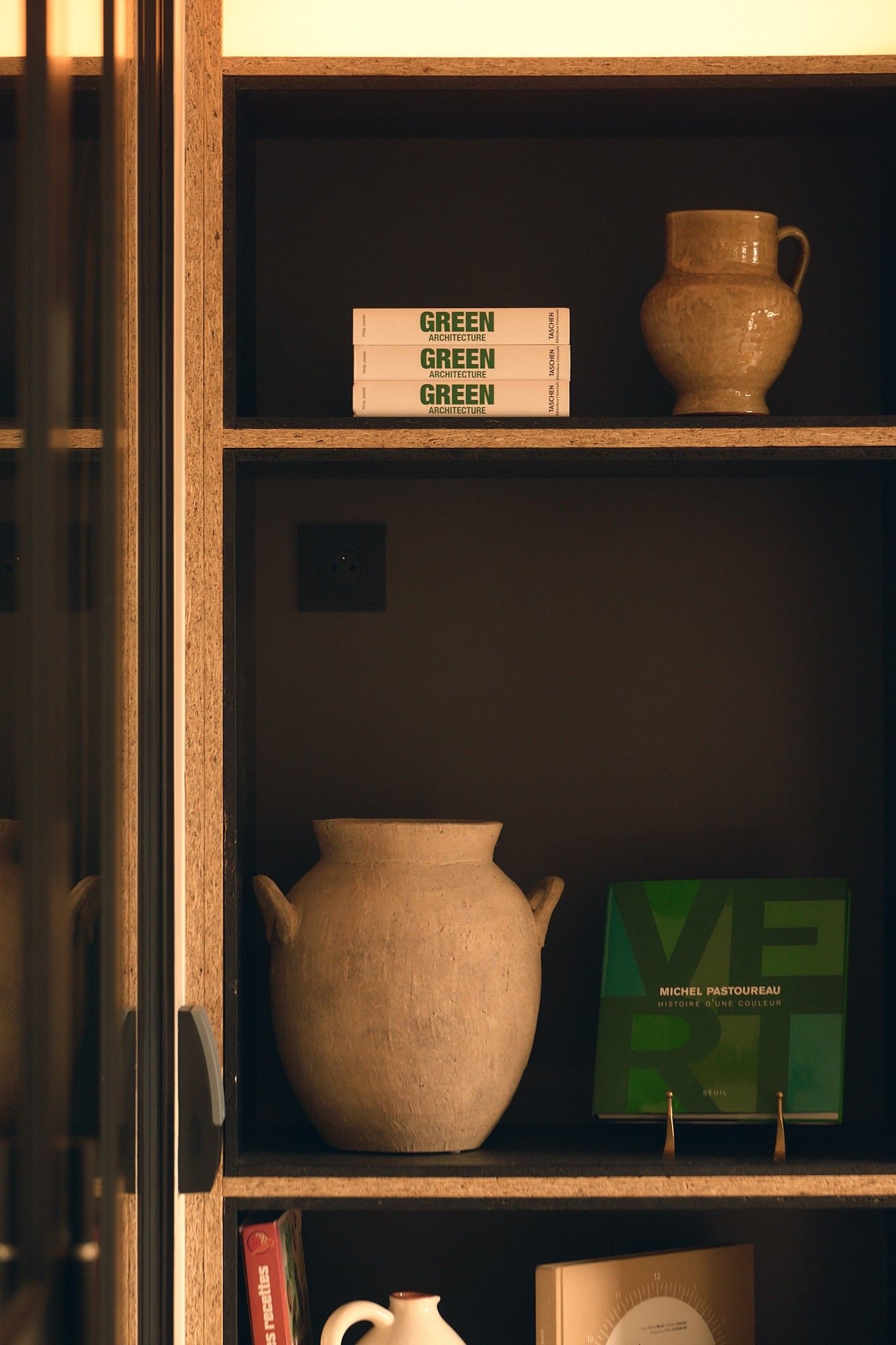 Une étagère avec un vase, un livre intitulé « ARCHITECTURE VERTE » et un livre de Michel Pastoureau.