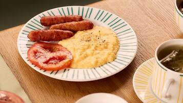 Un plato de desayuno con salchichas, huevos revueltos y una rodaja de tomate sobre un plato a rayas.