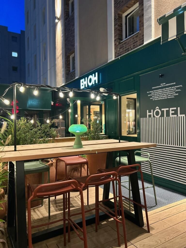 Un área de estar al aire libre con una mesa, sillas, luces colgantes y una lámpara verde.