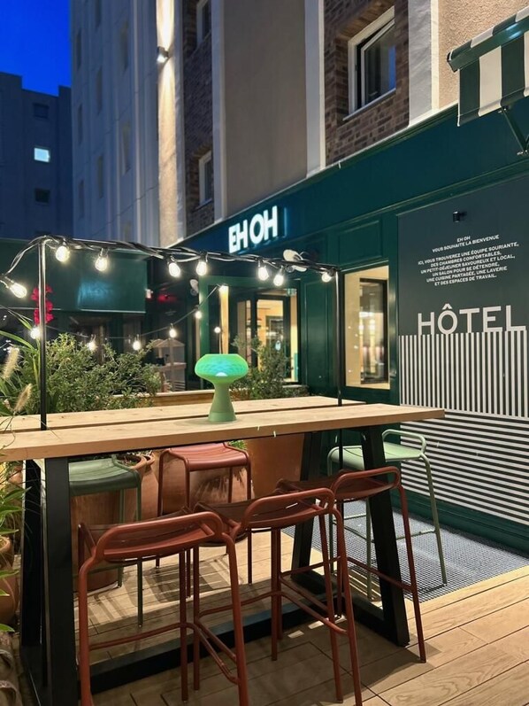 An outdoor seating area with a table and chairs, string lights, and a green lamp. - Hôtel EH OH Orly Rungis (Rungis)