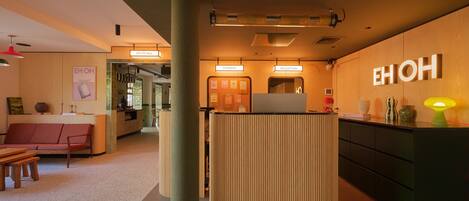 A reception area with a wooden reception desk, a seating area with a sofa and chairs, and a wall with a neon sign.