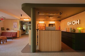 Un espace d'accueil comprenant un comptoir de réception en bois, un coin salon avec un canapé et des fauteuils, et un mur orné d'une enseigne au néon.