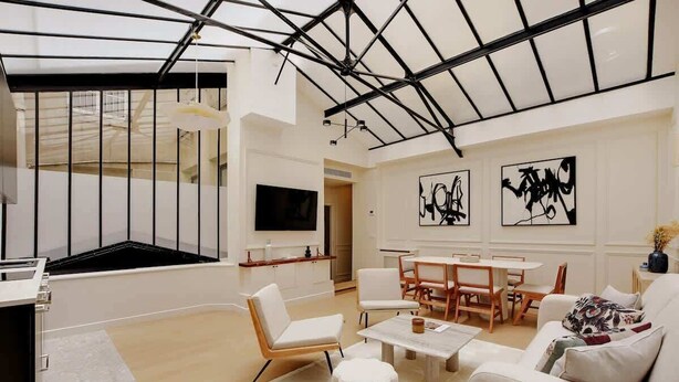 Ein modernes Wohnzimmer mit Glasdecke, weißen Möbeln und abstrakter Kunst an den Wänden.