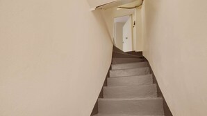 Eine enge Treppe mit Handlauf, die zu einer Tür oben führt.