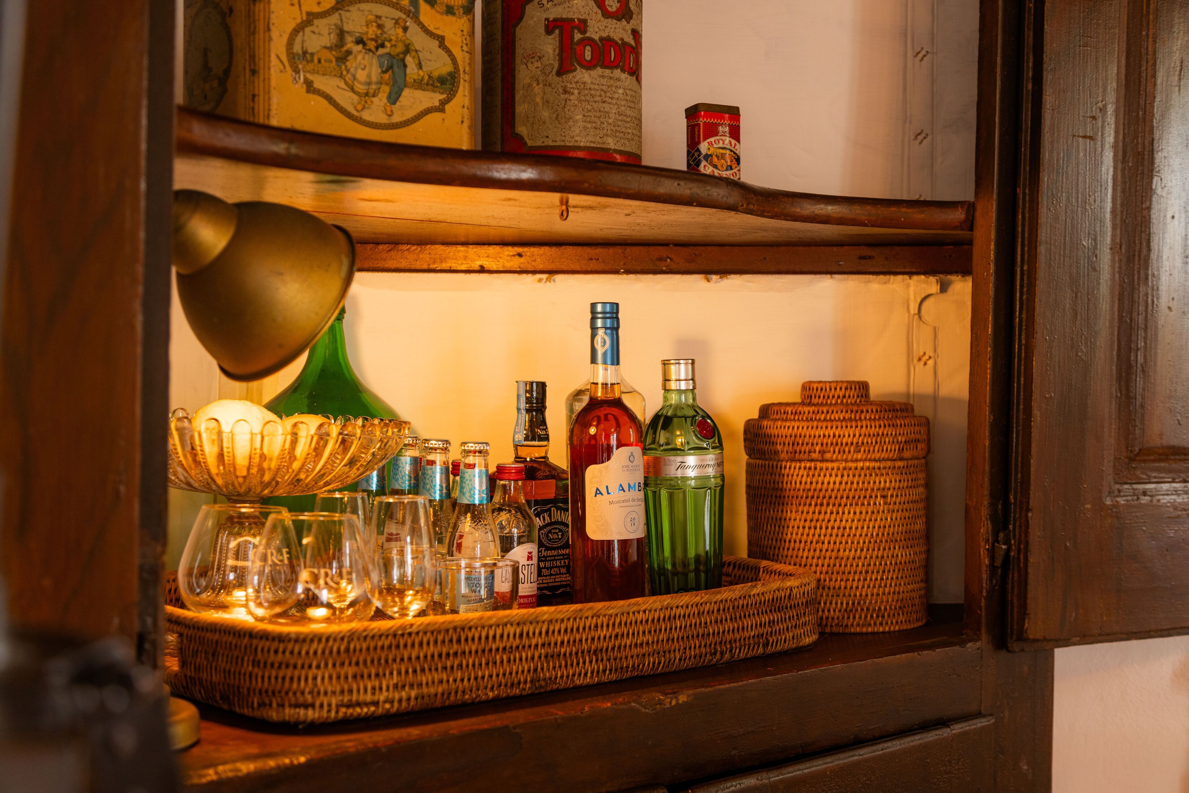 A shelf with various bottles and glasses, a green lamp, and a wicker basket.