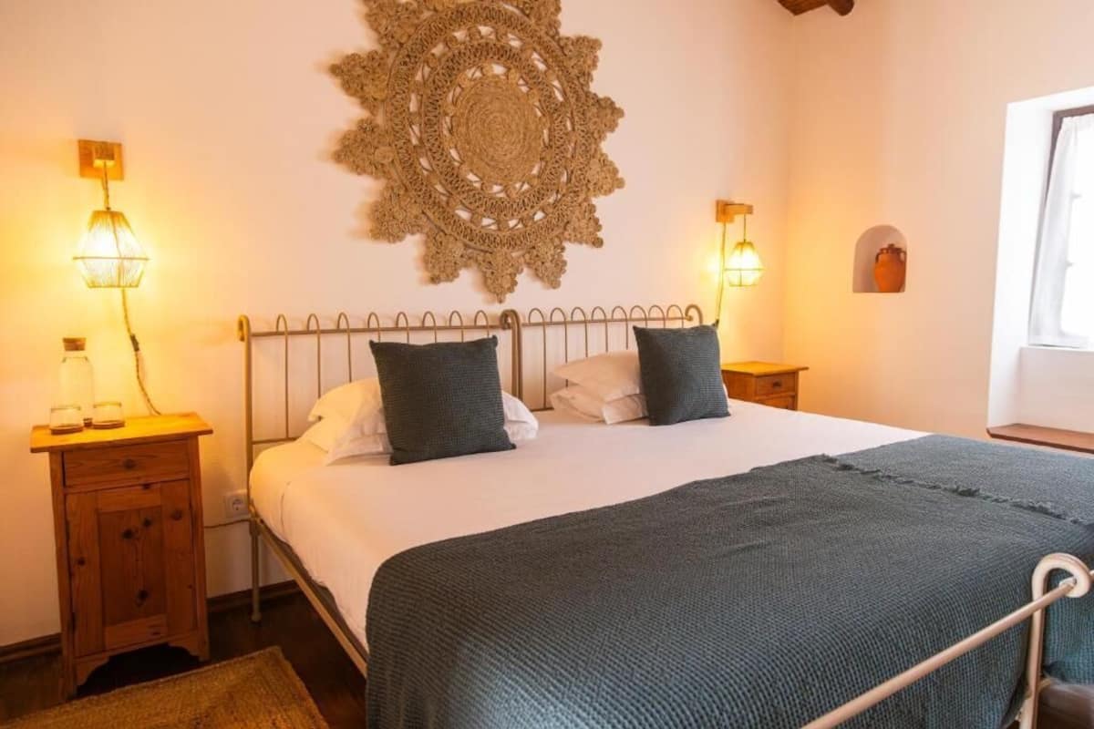 A bedroom with a metal bed frame, two bedside tables, a wall hanging, and a window.