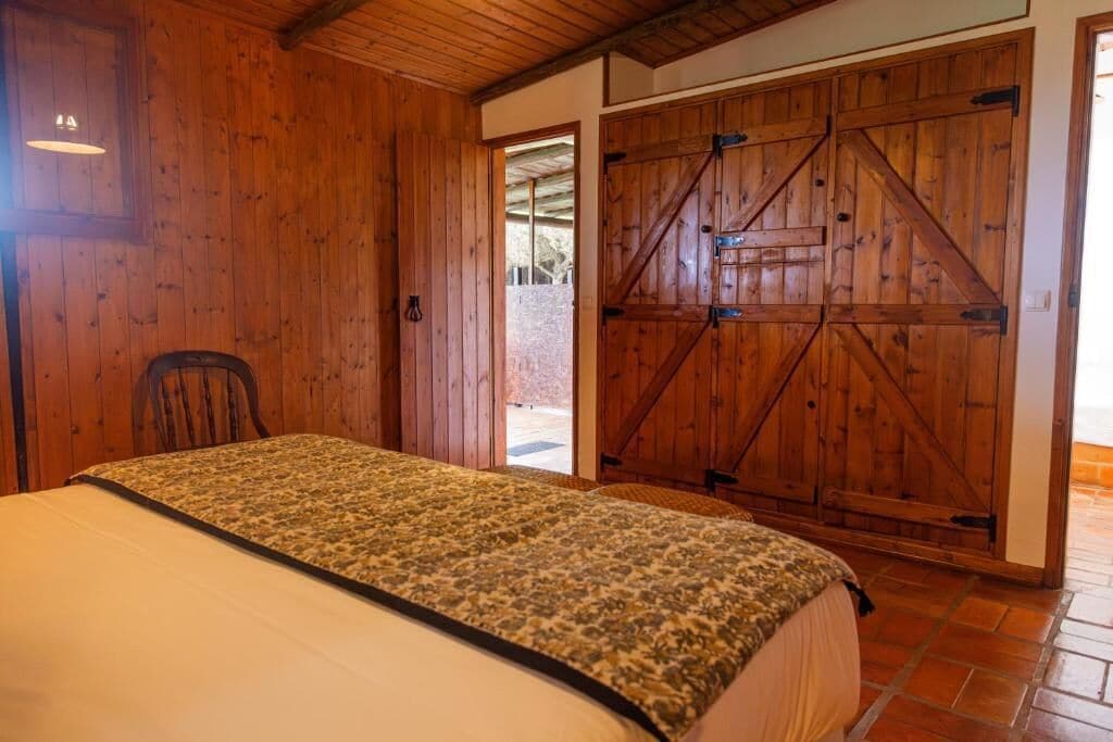 Un dormitorio con cama, paredes de madera, una silla y una amplia puerta de madera de granero.