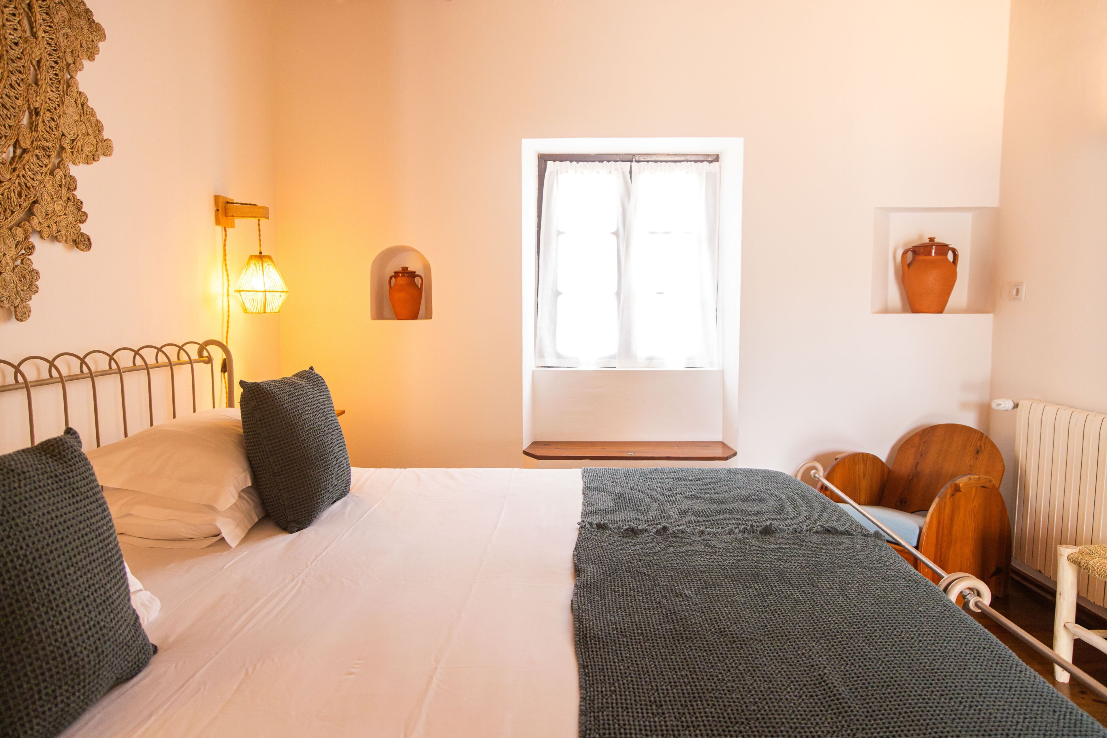 Een slaapkamer met een bed, een raam, een lamp, een plank met een vaas en een stoel.