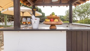 Una zona de bar con una mesa de madera, una botella de vino, copas y un frutero.