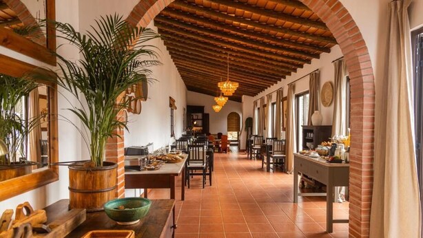 Un comedor espacioso con techo alto, arcos de ladrillo y una larga mesa con sillas.