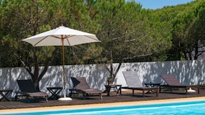 Zona junto a la piscina con sillones reclinables, una mesa y una sombrilla.