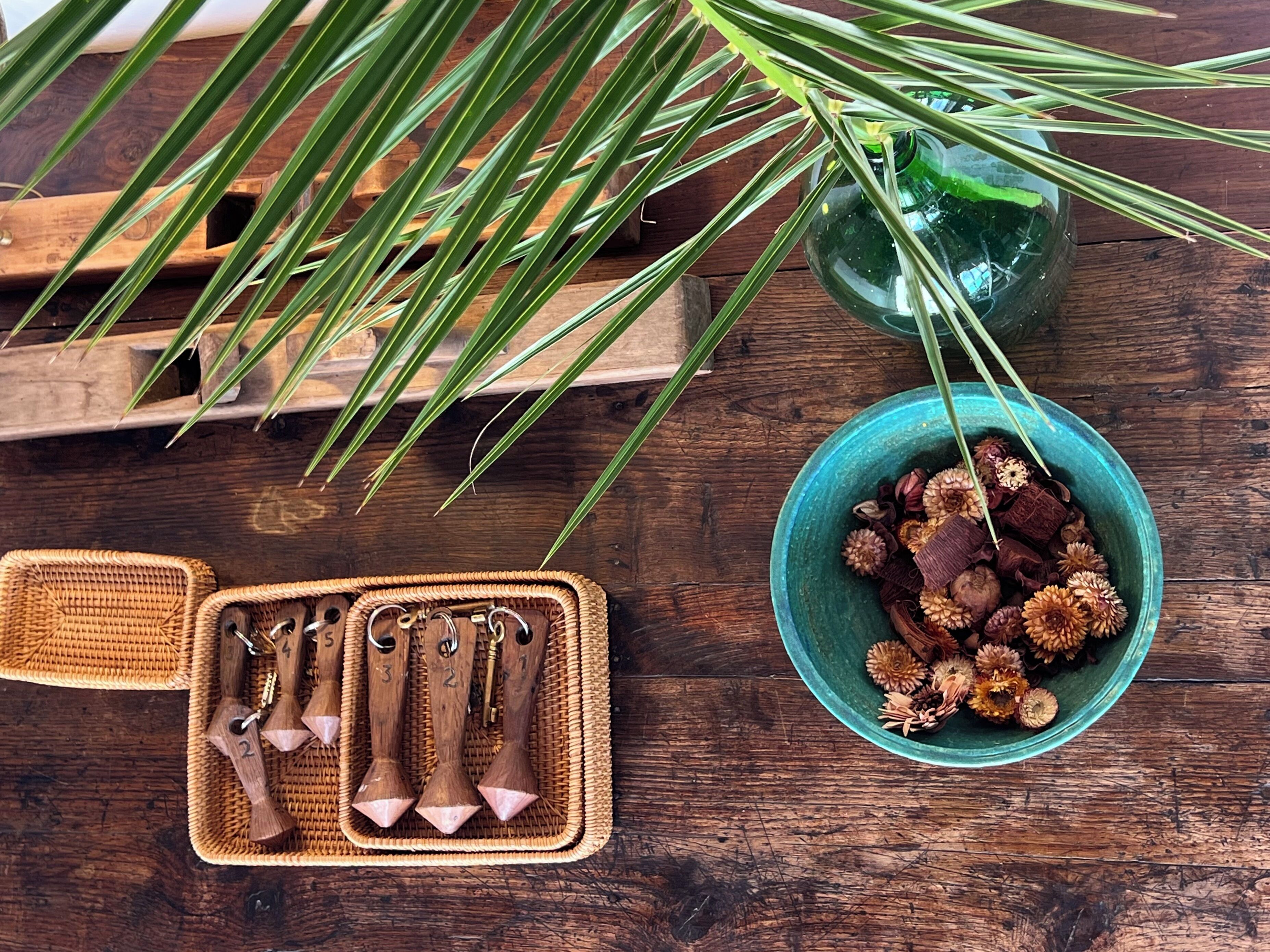 A wooden surface with a woven basket, a green bowl with dried flowers, and a green glass bottle.