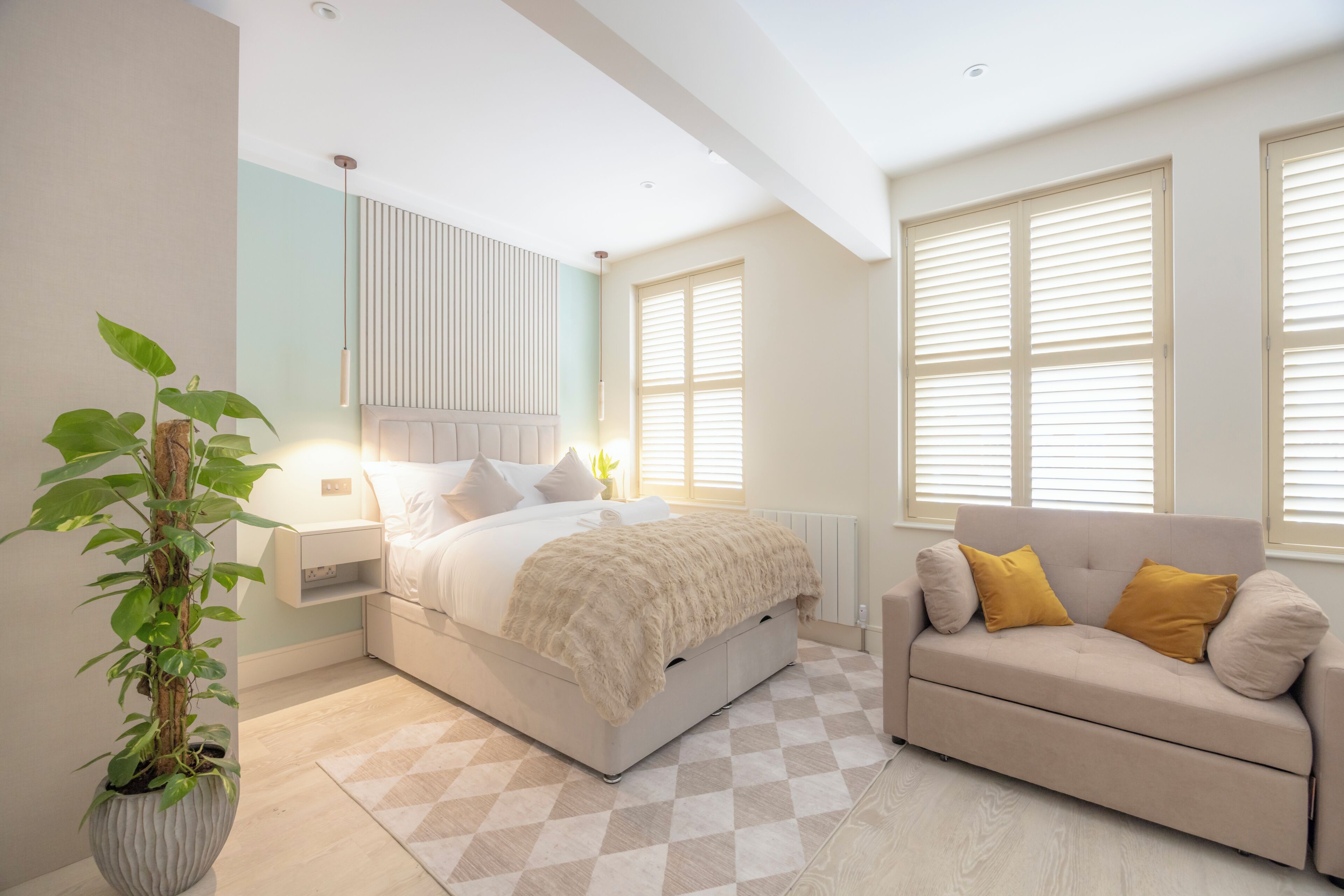 Een slaapkamer met een bed, nachtkastje, plant in pot en een bank.