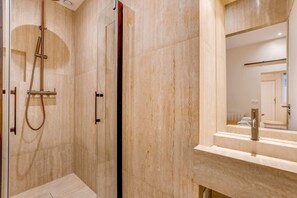 Ein modernes Badezimmer mit einer gläsernen Duschkabine, einem großen Spiegel und einer Wand mit Marmorfliesen.