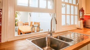 Une cuisine dotée d’un grand évier en acier inoxydable à deux bacs, de plans de travail en bois et de grandes fenêtres.