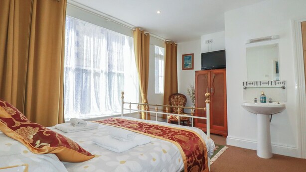 Une chambre d’hôtel comprenant un lit, une table de chevet, une fenêtre avec des rideaux, une télévision, une armoire et une salle de bain avec un lavabo et un miroir.