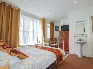 Een hotelkamer met een bed, nachtkastje, raam met gordijnen, televisie, kledingkast en een badkamer met wastafel en spiegel.