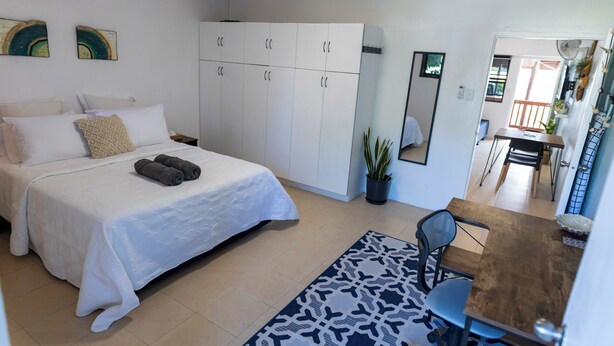 Un dormitorio con cama, armario, escritorio, silla y zona de comedor.