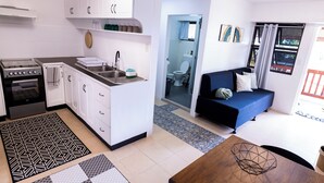 Un espacio habitable compacto con kitchenette, comedor, sofá y vistas al exterior.