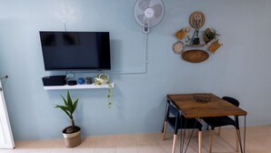 Sala de estar con televisor, ventilador, mesa con sillas, planta en maceta y adornos en la pared.