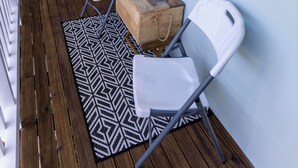 Una terraza de madera con dos sillas blancas, una mesa pequeña y plantas en macetas.