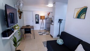 Un espacio habitable compacto con televisor, mesa de comedor, sofá, refrigerador, ventilador y una planta en maceta.