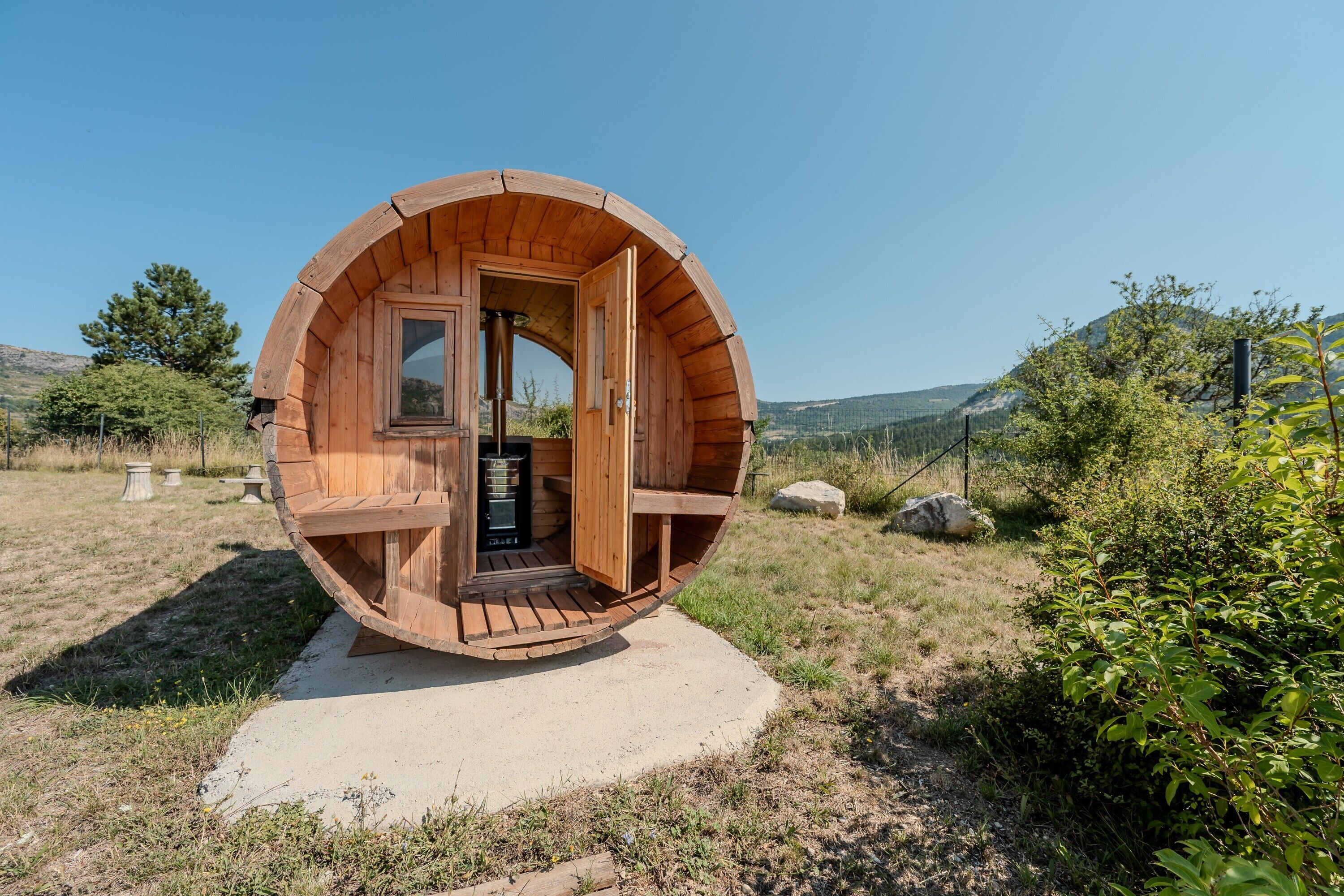 Una estructura en forma de barril de madera, con una puerta y escalones que conducen a ella, mostrando una vista del paisaje circundante.