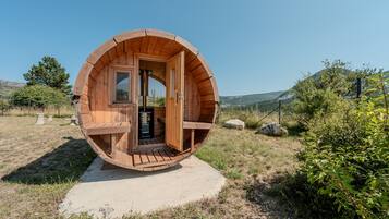 Una estructura en forma de barril de madera, con una puerta y escalones que conducen a ella, mostrando una vista del paisaje circundante.