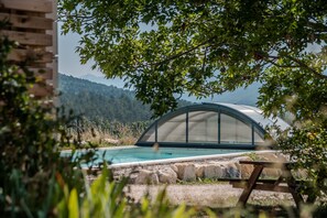 A swimming pool with a semi-circular glass enclosure, surrounded by natural landscape and vegetation. - Apartment with Private Terrace and Pool (Mévouillon)