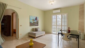 Ein Wohnzimmer mit einer Couch, einem Esstisch mit Stühlen, einem Gemälde an der Wand und einem großen Fenster.