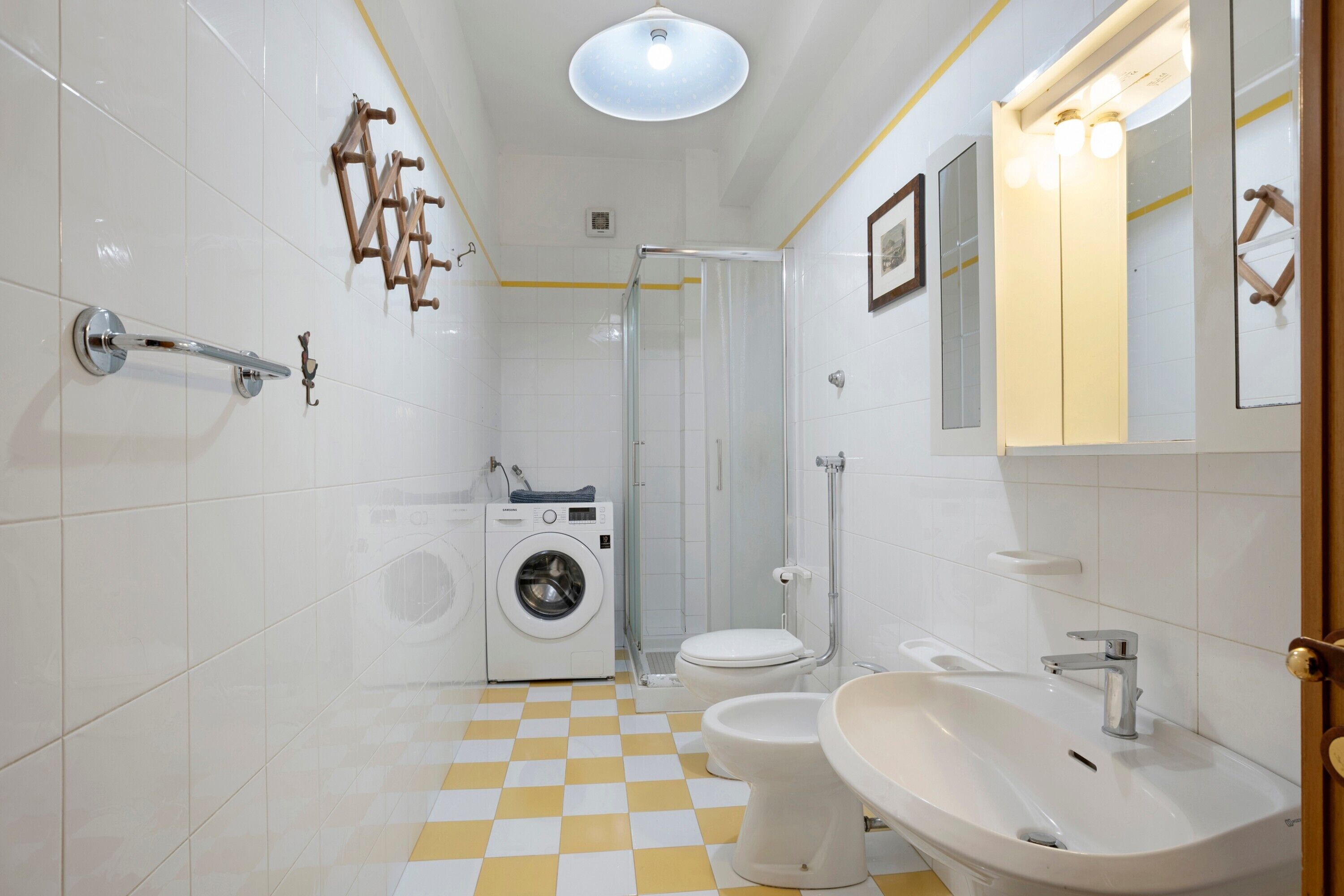 Ein Badezimmer mit Schachbrettboden, einer Waschmaschine, einer Toilette, einem Waschbecken und einer Dusche.