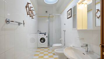 Ein Badezimmer mit Schachbrettboden, einer Waschmaschine, einer Toilette, einem Waschbecken und einer Dusche.
