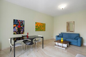 Un salon comprenant une table à manger, des chaises, un canapé bleu et deux tableaux abstraits accrochés au mur.