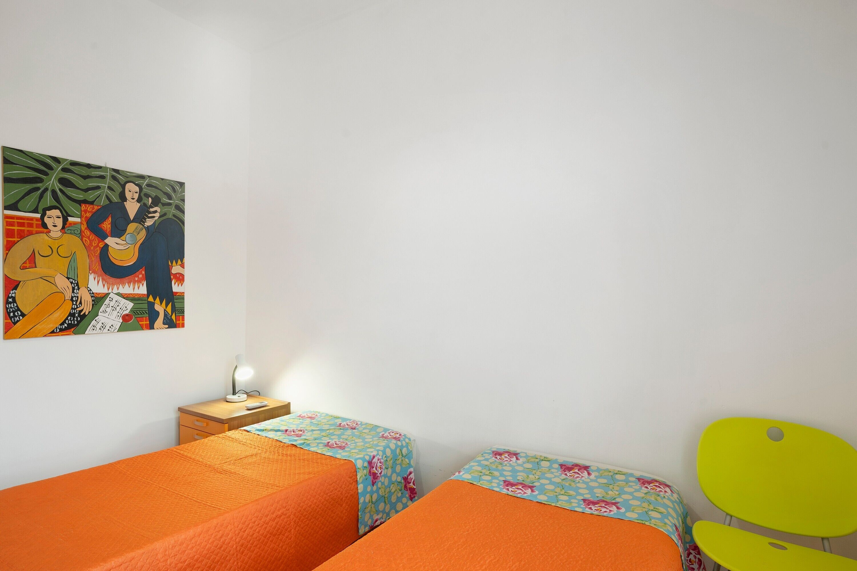 A room with two beds, a nightstand with a lamp, a painting on the wall, and a chair.