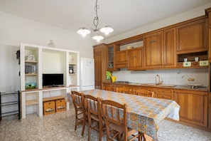 Een keuken met houten kastjes, een ingebouwde televisie, een eettafel met stoelen en een kroonluchter.