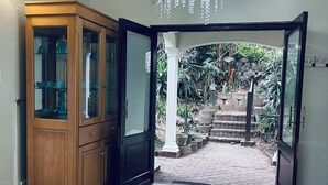 A room with a wooden cabinet, a chandelier, and a view of a garden through an open door. - Selborne Golf Estate Villa P15 (Pennington)